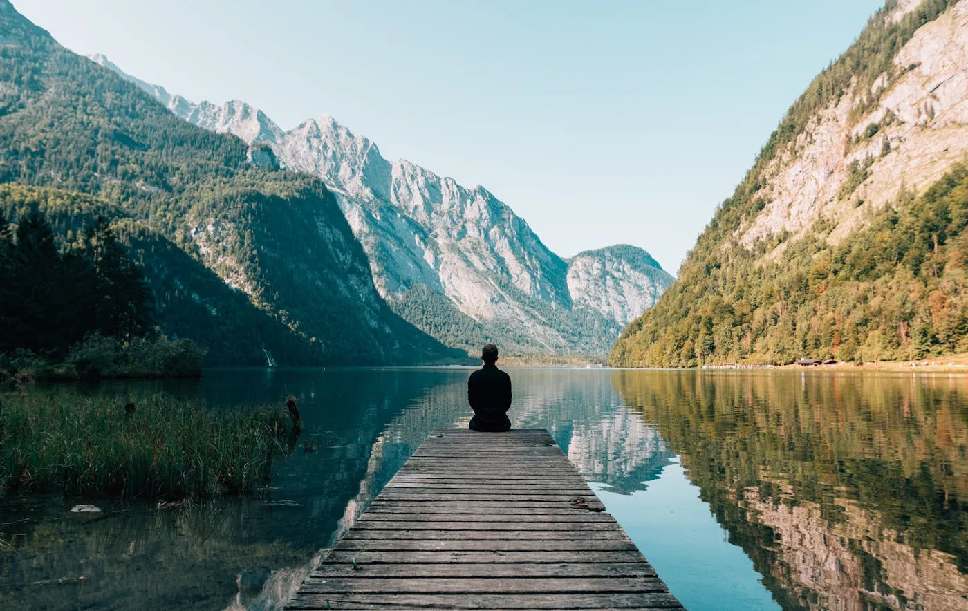 Person meditating peacefully by a mountain lake